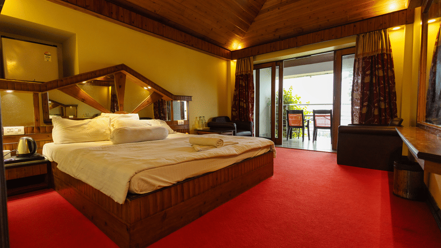 A bedroom with a king size bed, seating area, red carpet, and open balcony door at Hotel Seagull Digha.